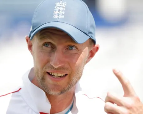 England captain Joe Root, wearing a blue England cap, smiles and gestures during a TV interview